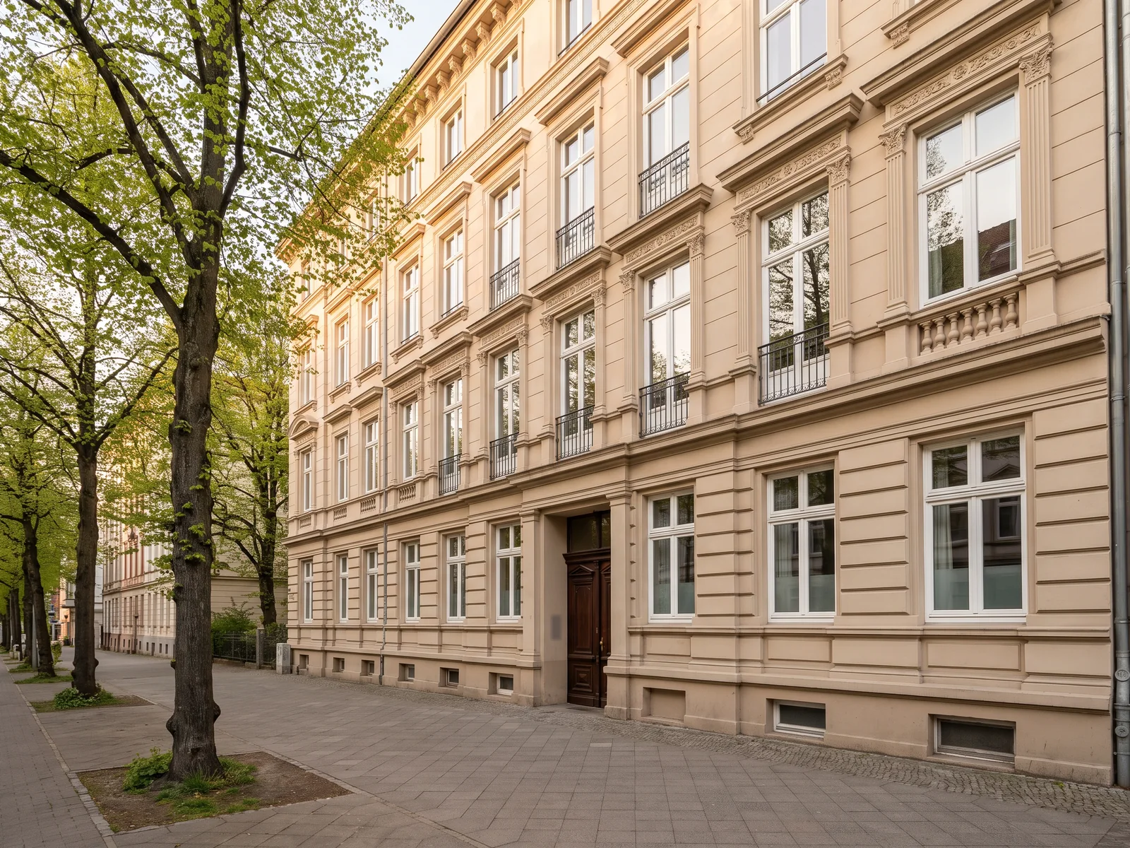 Gründerzeitfassade mit Balkonen hinter Straßenbäumen, illustratives Motiv